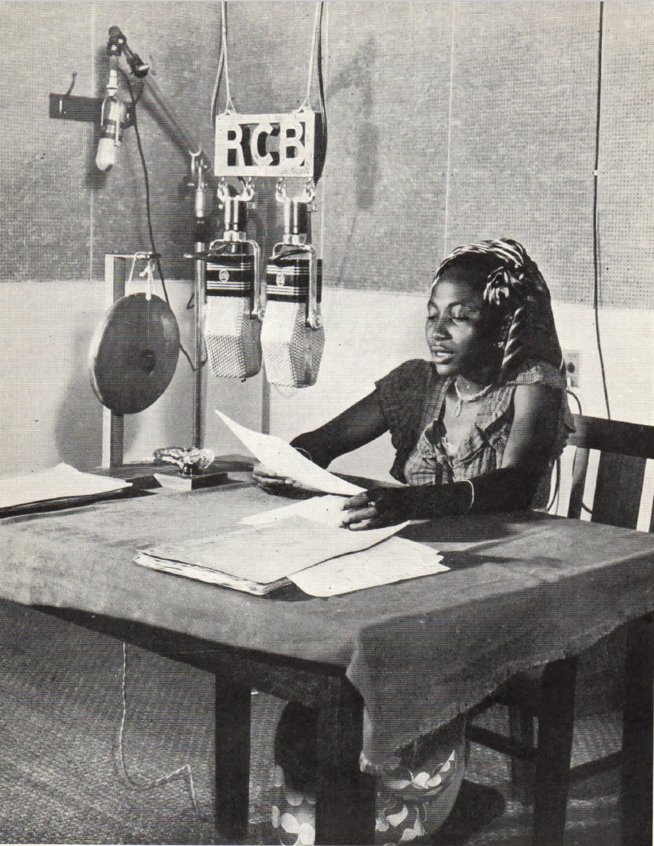 Woman sitting at a table in front of microphones, reading from a paper